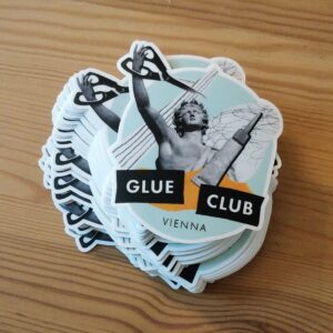 Ein Stapel Vinylsticker mit Glue Club Vienna Logo, die auf einem Holzuntergrund liegen.